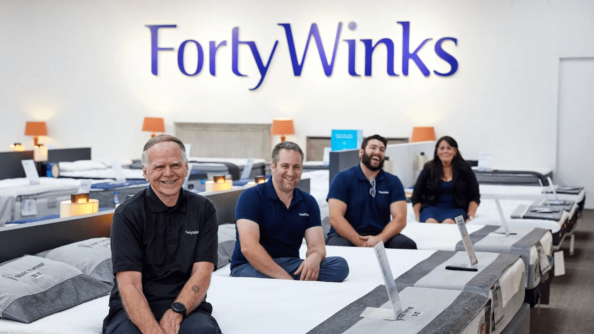 Four Forty Winks franchisees seated on mattresses under the store logo